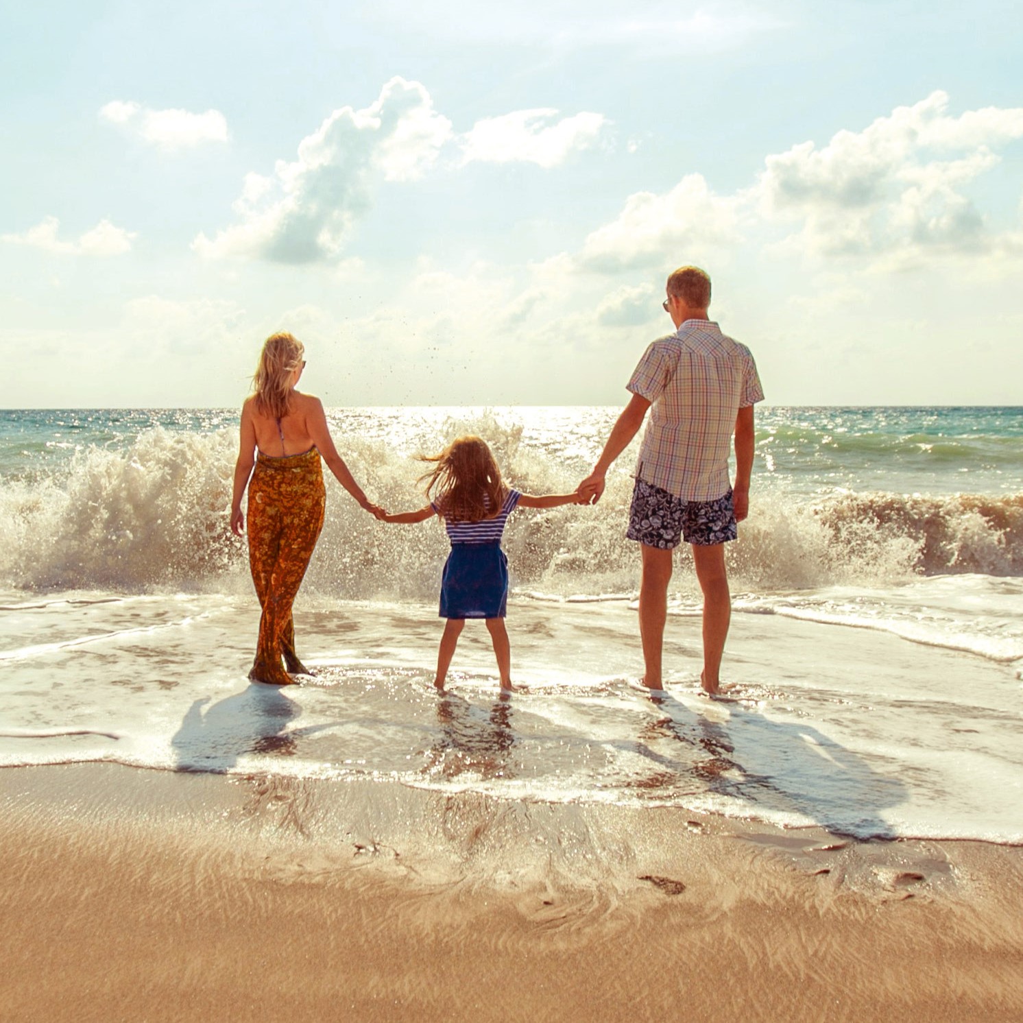 natalya-zaritskaya-SIOdjcYotms-unsplash Eine junge Familie steht händchenhaltend mit dem Rücken zur Kamera in der Gischt am Strand